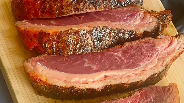 Grilled picanha sliced on a cutting board, showing a pink center under the browned fat cap, at Costa's Meat Market